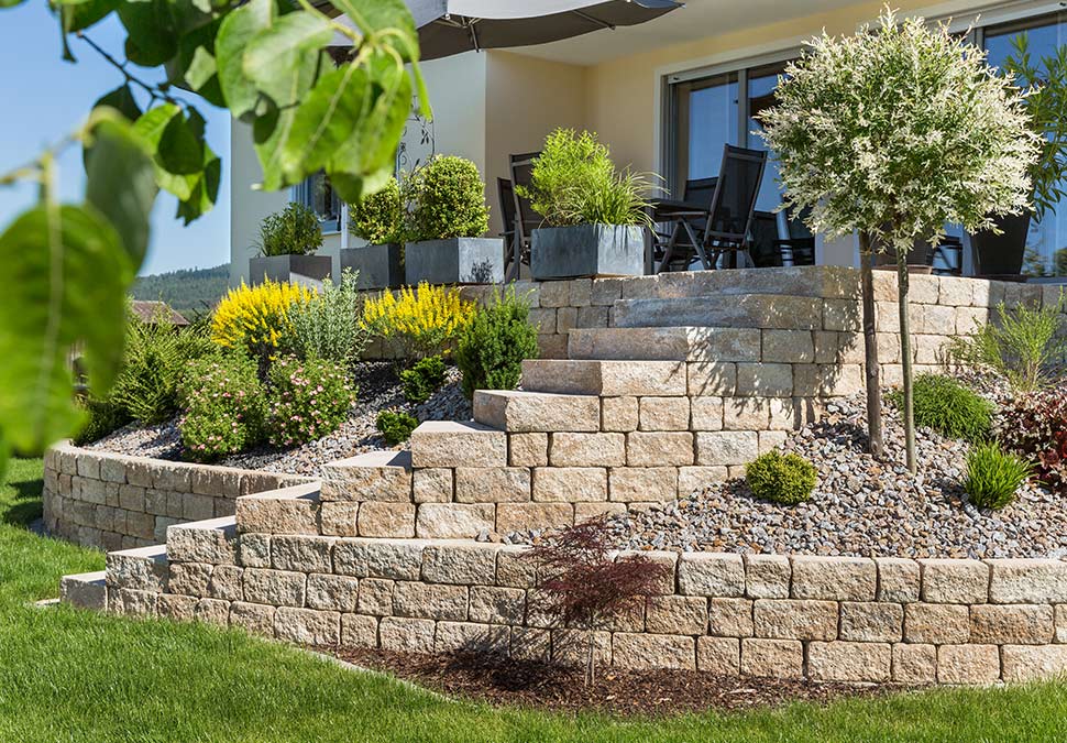 Bepflanzte Gartenterrasse mit Hangbefestigung und Treppenanlage mit hellen Mauersteinen | Garten- und Landschaftsbau | Bauzentrum Zillinger